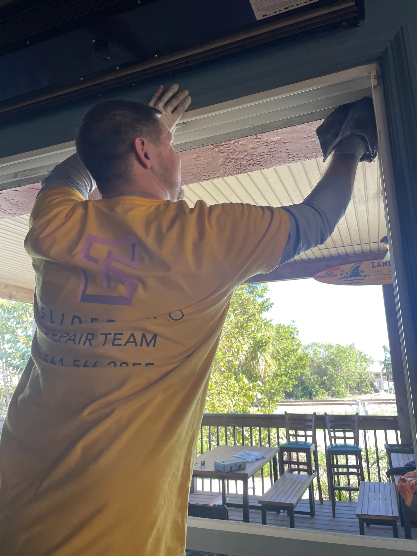 SliderPro technician in a branded repair-team shirt working along the head track of a sliding door
