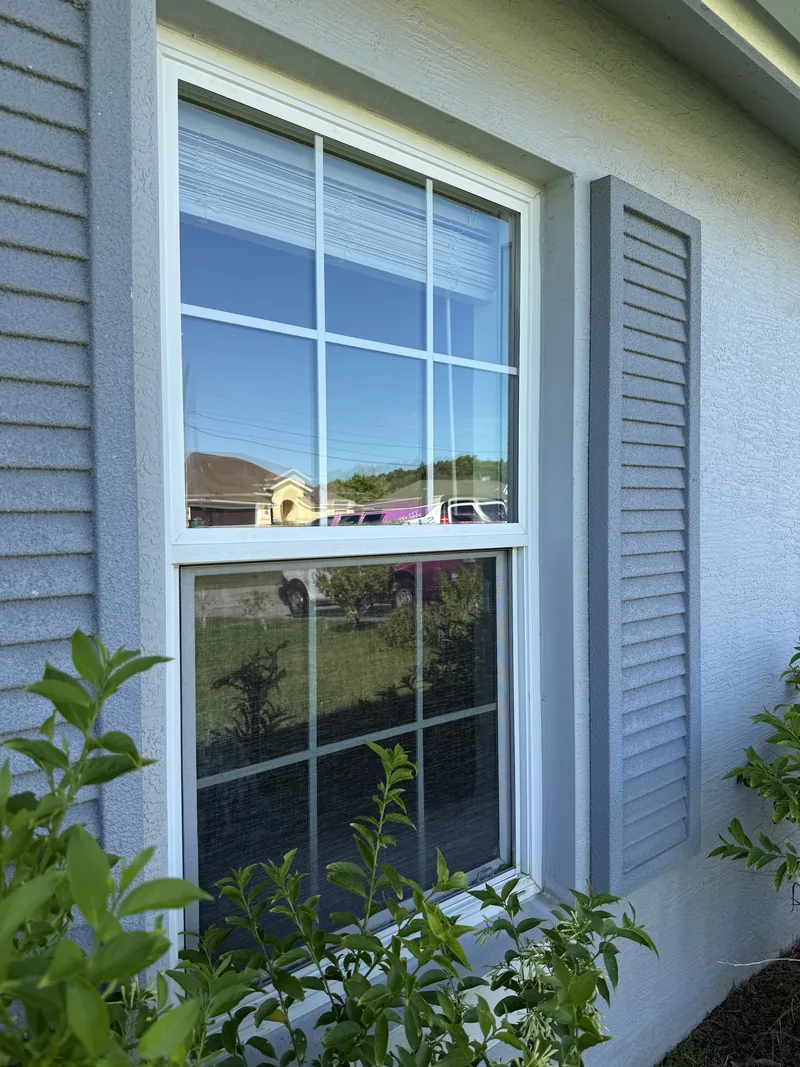 The same window after replacement, with a clear low-E insulated impact unit and matching colonial grid in the original frame